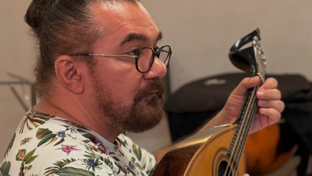 Imagem colorida mostra o instrumentista Rosivaldo Cordeiro tocando um banjo e olhando para pessoas que estão a sua frente aprendendo sobre o instrumento