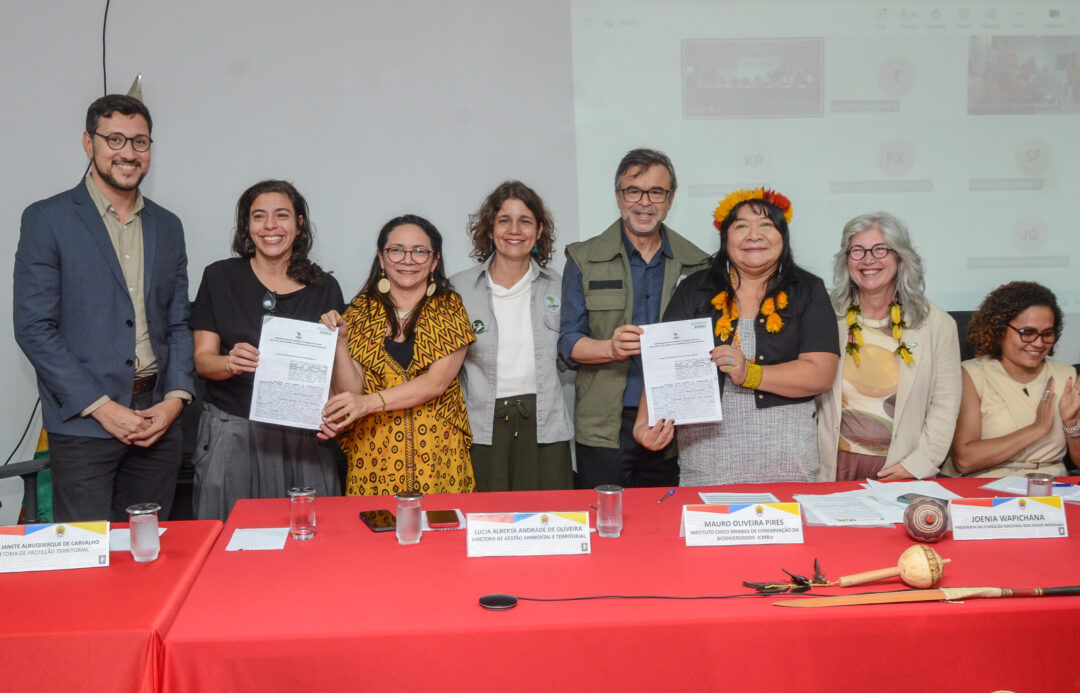 Imagem colorida mostra ICMbio e Funai firmando acordo com líderes mostrando papeis assinados