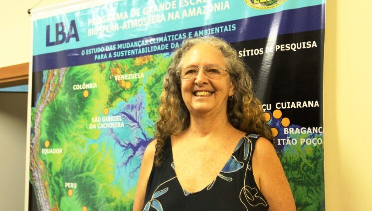 Imagem colorida mostra a socioambientalista Muriel Saragoussi sorrindo em uma apresentação com uma mapa da america do sul ao fundo