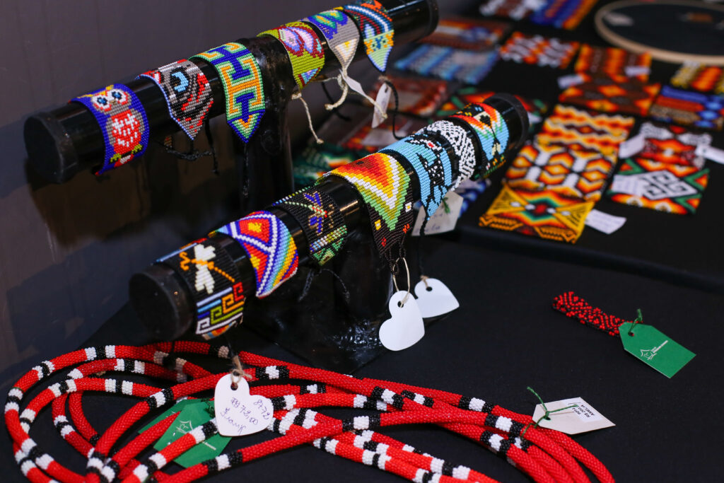 Imagem colorida mostra artesanatos expostos em mesa preta