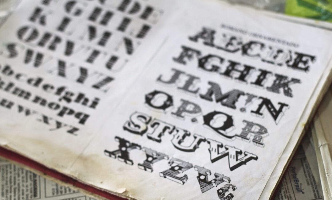 Imagem colorida mostra caderno aberto com letras do alfabeto em diferente tipografias