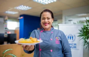 Imagem colorida mostra a empreendedora refugiada Ana Joselyn servindo prato feito por ela em uma espaço em Manaus