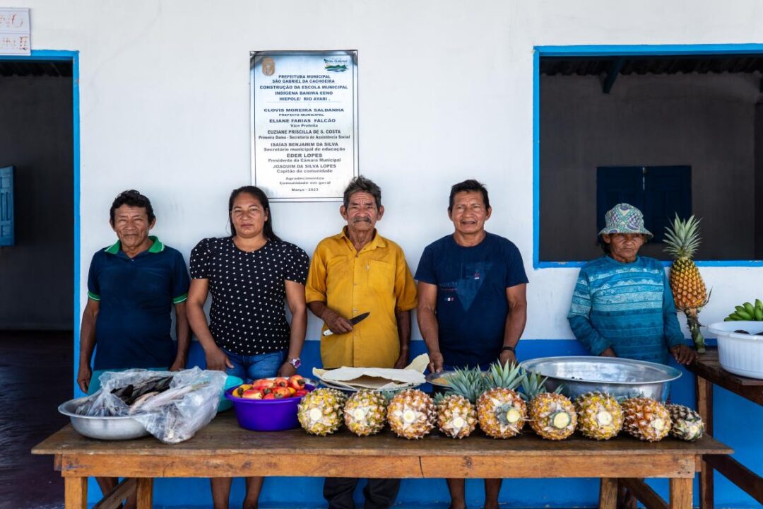 Imagem colorida mostra família indígena entregando alimentação escola em escola no Amazonas
