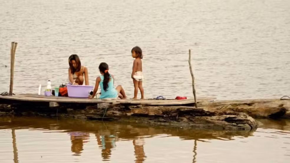 Imagem colorida mostra mãe e crianças ribeirinhas em área de rios com poucas terras para falar sobre dados da Unicef